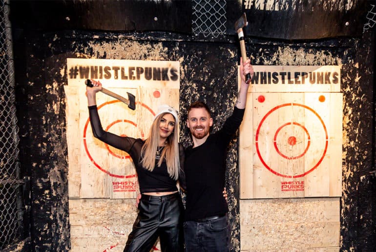 A man and woman holding throwing axes up