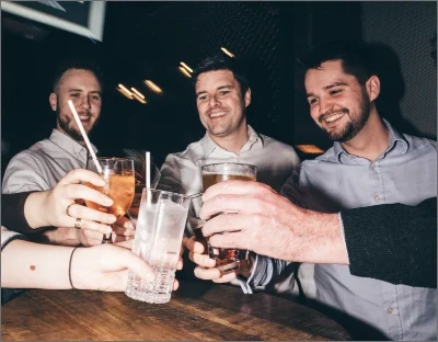 A group of men stood in a circle, smiling and cheersing glasses.